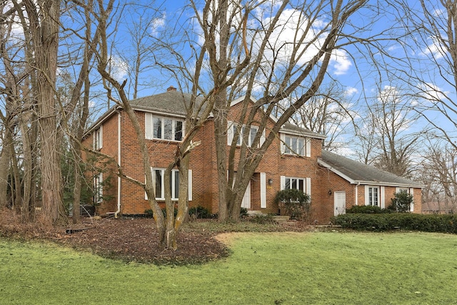 view of front of home featuring brick siding, a chimney, and a front lawn