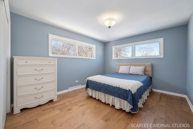 bedroom featuring a baseboard heating unit, light wood-style flooring, and baseboards