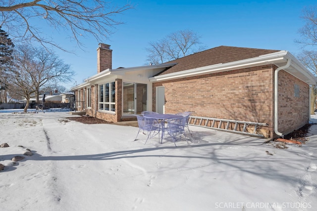 snow covered house featuring outdoor dining space, brick siding, and a chimney