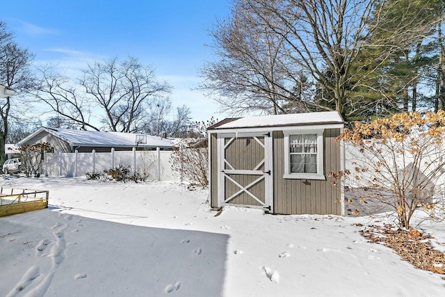 snow covered structure with an outbuilding, a shed, and fence