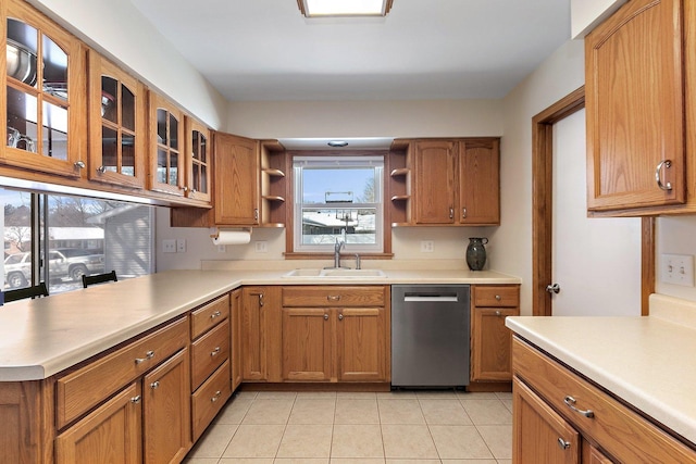 kitchen featuring light countertops, stainless steel dishwasher, a sink, and glass insert cabinets