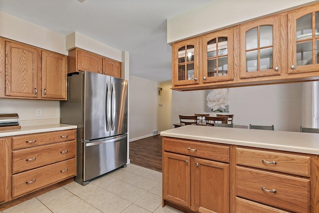 kitchen featuring light countertops, brown cabinetry, glass insert cabinets, and freestanding refrigerator