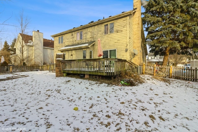 snow covered back of property with a chimney, fence, and a wooden deck