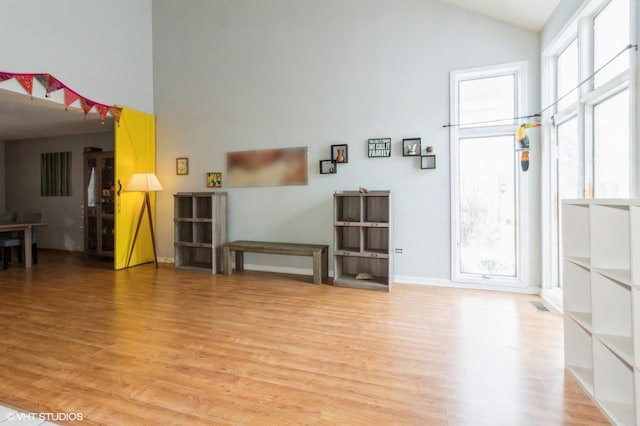 interior space with light wood-type flooring, baseboards, visible vents, and high vaulted ceiling