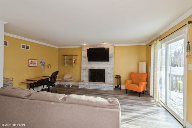 living area with ornamental molding, a brick fireplace, visible vents, and wood finished floors