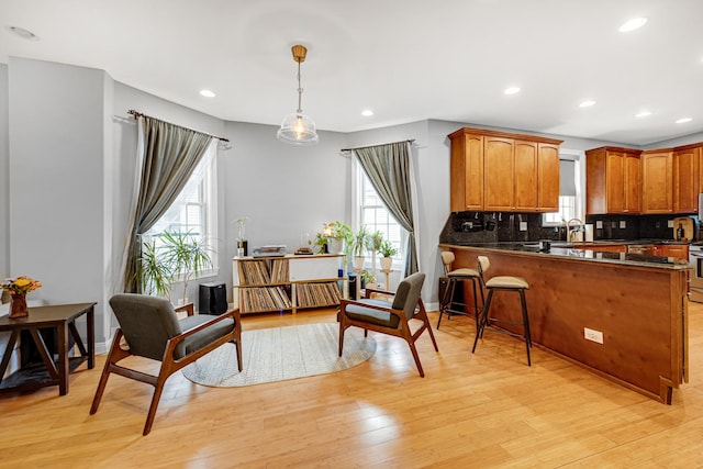 kitchen featuring light wood-style flooring, decorative backsplash, brown cabinetry, dark countertops, and decorative light fixtures