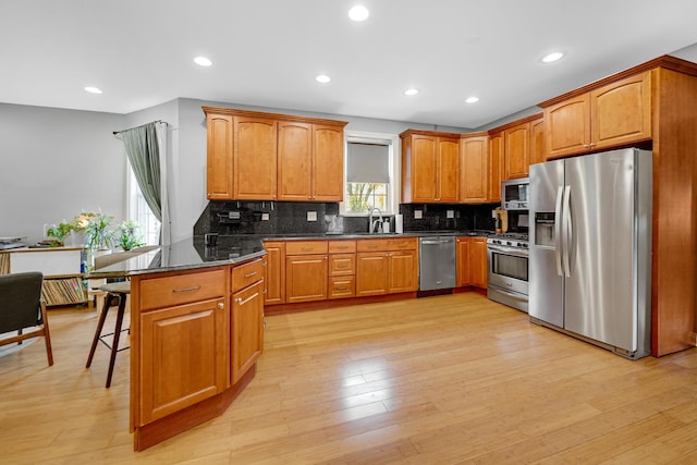 kitchen featuring stainless steel appliances, brown cabinetry, light wood-style floors, and a kitchen bar