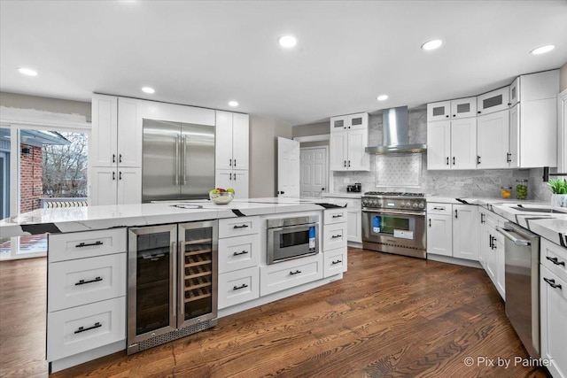 kitchen with high end appliances, wine cooler, white cabinets, and wall chimney range hood