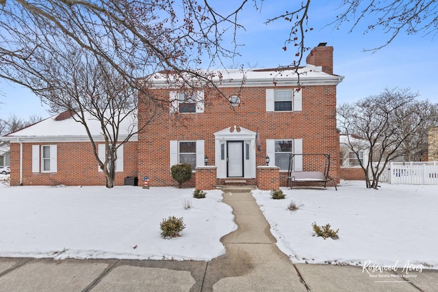 colonial house featuring a chimney and brick siding