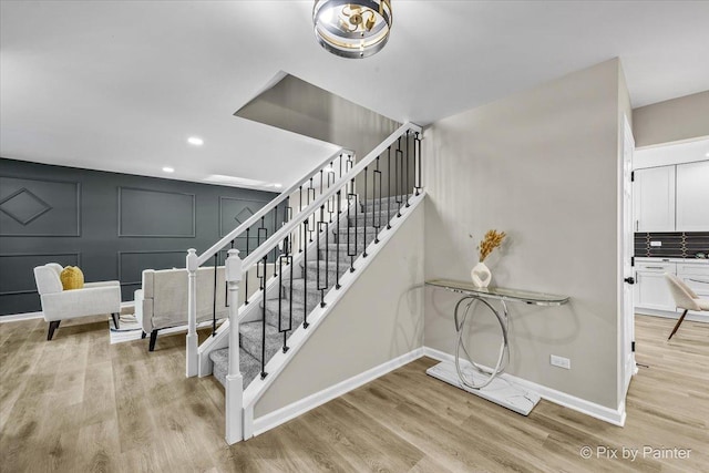 stairs with baseboards, a decorative wall, wood finished floors, and recessed lighting