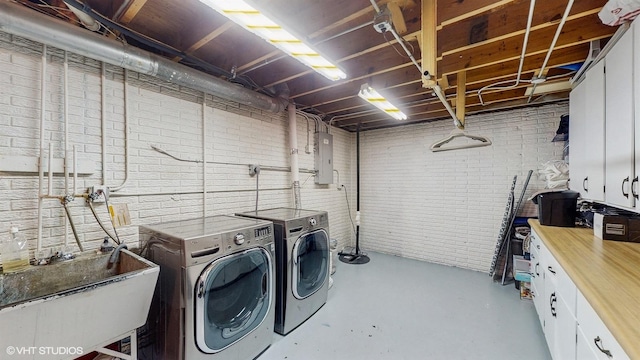 clothes washing area featuring cabinet space, electric panel, brick wall, independent washer and dryer, and a sink