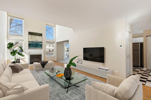 living area with light wood-type flooring, baseboards, a fireplace, and a high ceiling