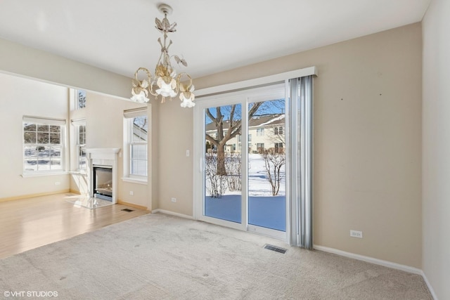 unfurnished dining area with light carpet, a wealth of natural light, a fireplace with flush hearth, and visible vents