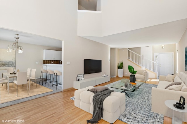 living area featuring a chandelier, stairway, light wood-style flooring, and a high ceiling