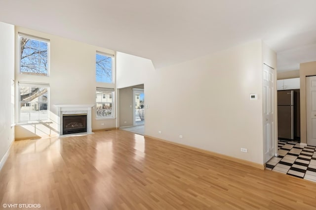 unfurnished living room featuring baseboards, a high ceiling, a high end fireplace, and light wood-style floors