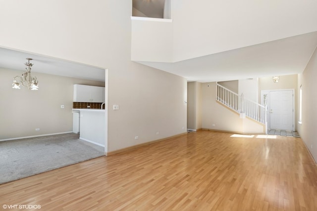 unfurnished living room featuring a high ceiling, an inviting chandelier, light wood-style floors, baseboards, and stairs