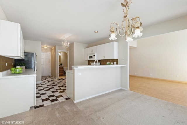 kitchen with pendant lighting, light countertops, white microwave, an inviting chandelier, and white cabinetry