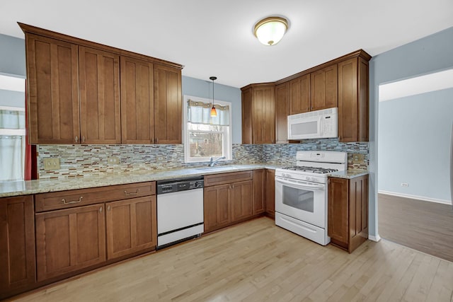 kitchen with white appliances, light wood-style flooring, backsplash, and a sink