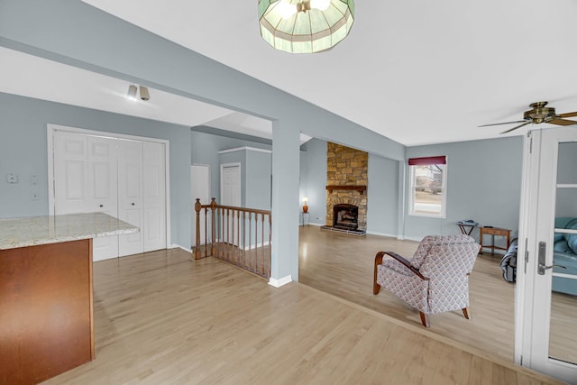 interior space with light wood finished floors, baseboards, a ceiling fan, and a stone fireplace