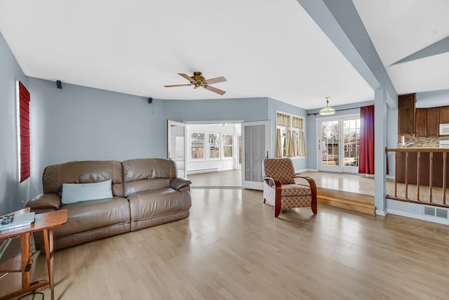 living room featuring light wood-style floors, baseboards, visible vents, and a ceiling fan