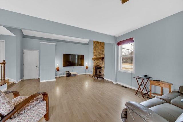 living room featuring a stone fireplace, wood finished floors, visible vents, and baseboards