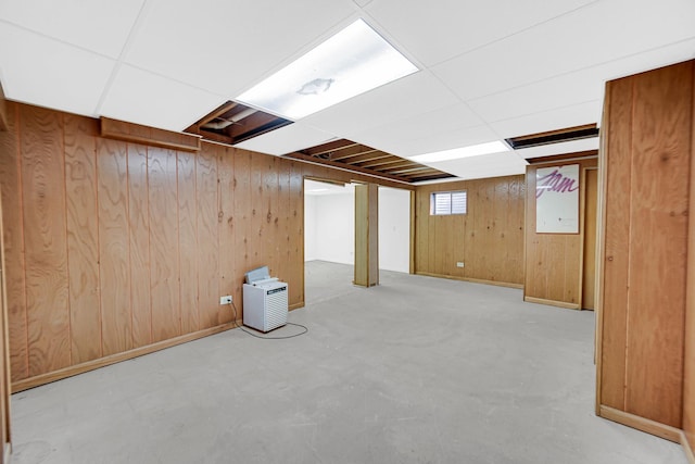 basement featuring a drop ceiling, wooden walls, and baseboards