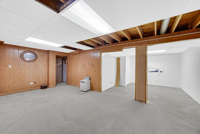 finished below grade area featuring water heater, baseboards, and wooden walls