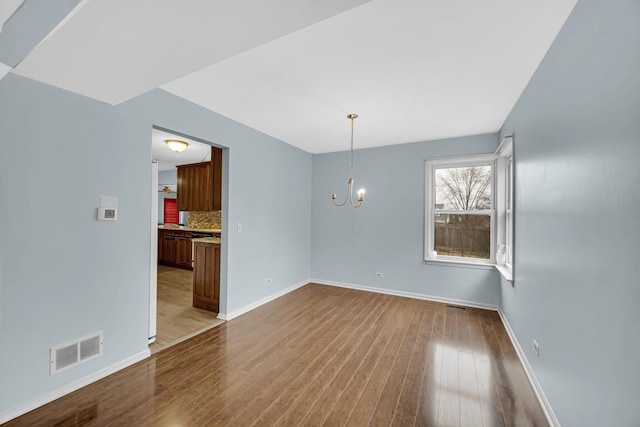 unfurnished dining area with dark wood-style floors, baseboards, visible vents, and a notable chandelier