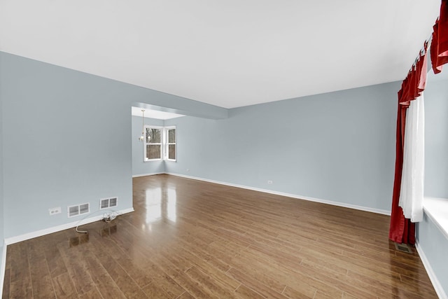 unfurnished living room with visible vents, a notable chandelier, baseboards, and wood finished floors