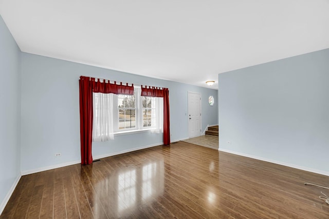 unfurnished living room featuring stairs, dark wood-style flooring, and baseboards