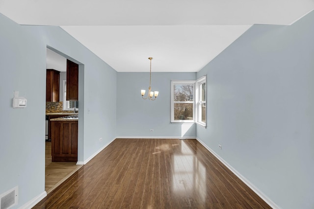 unfurnished dining area with dark wood-type flooring, visible vents, a notable chandelier, and baseboards