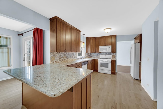 kitchen with white appliances, decorative backsplash, light wood-style flooring, light stone counters, and a peninsula