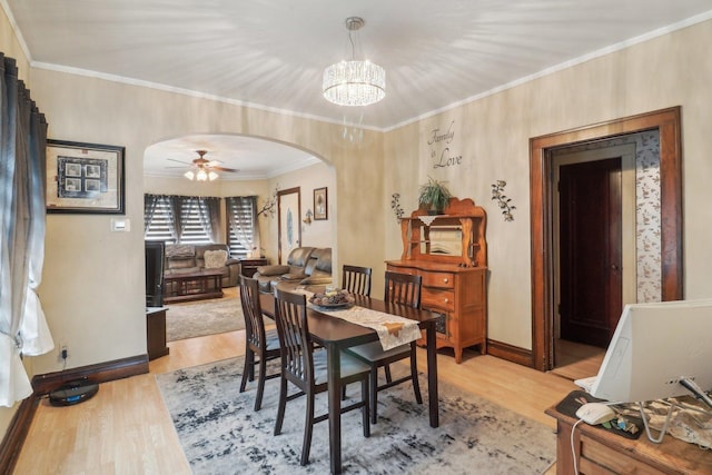 dining space featuring arched walkways, ceiling fan with notable chandelier, wood finished floors, baseboards, and ornamental molding