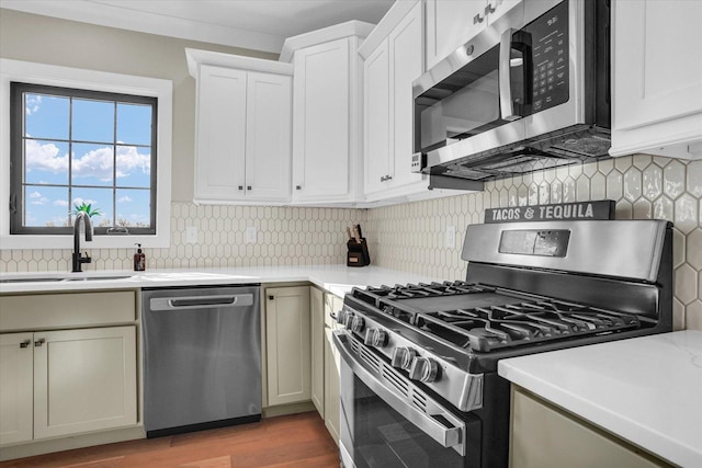 kitchen with light wood-style flooring, appliances with stainless steel finishes, a sink, light countertops, and backsplash