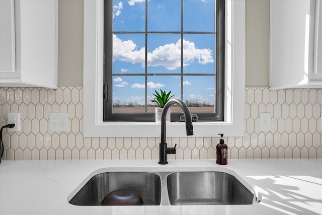 interior details featuring light stone counters, a sink, white cabinetry, and tasteful backsplash