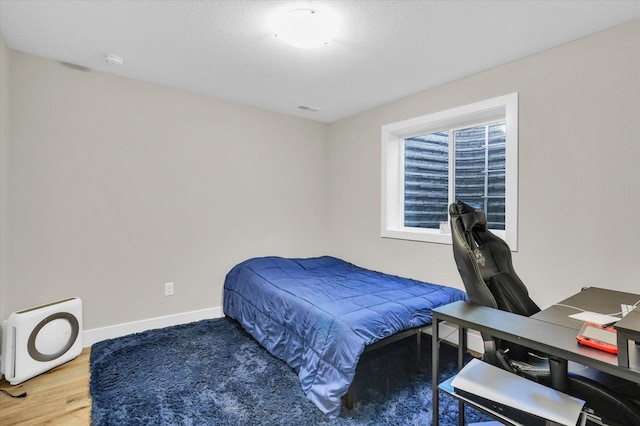 bedroom with a textured ceiling, wood finished floors, visible vents, baseboards, and heating unit