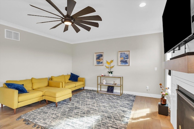 living room with baseboards, visible vents, ornamental molding, wood finished floors, and a fireplace