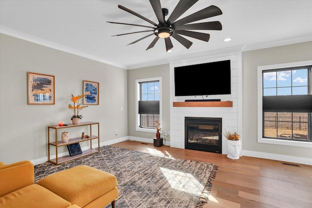 living room featuring crown molding, a large fireplace, ceiling fan, wood finished floors, and baseboards