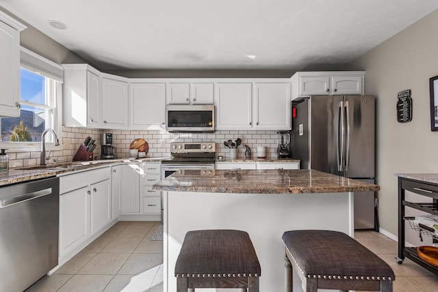 kitchen featuring light tile patterned floors, a sink, appliances with stainless steel finishes, tasteful backsplash, and dark stone countertops