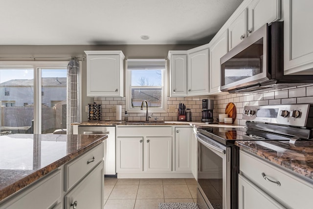 kitchen featuring light tile patterned floors, stainless steel appliances, backsplash, a sink, and dark stone counters