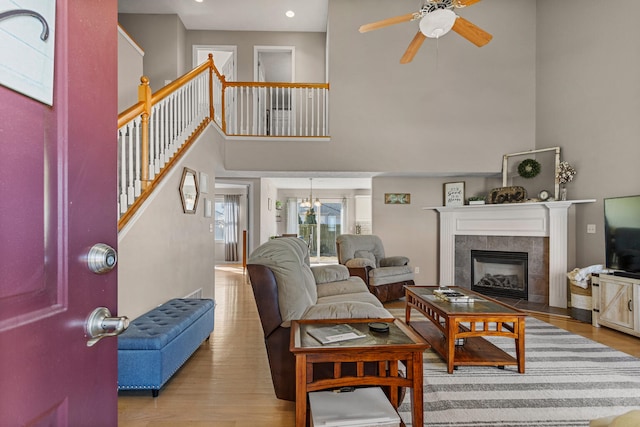 living area with ceiling fan, wood finished floors, stairs, a high ceiling, and a fireplace