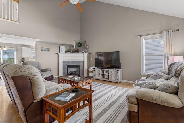 living room with high vaulted ceiling, a tile fireplace, light wood-style flooring, and a ceiling fan