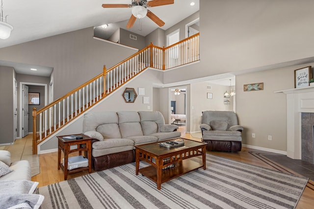 living area featuring baseboards, a tiled fireplace, ceiling fan, stairs, and light wood-type flooring