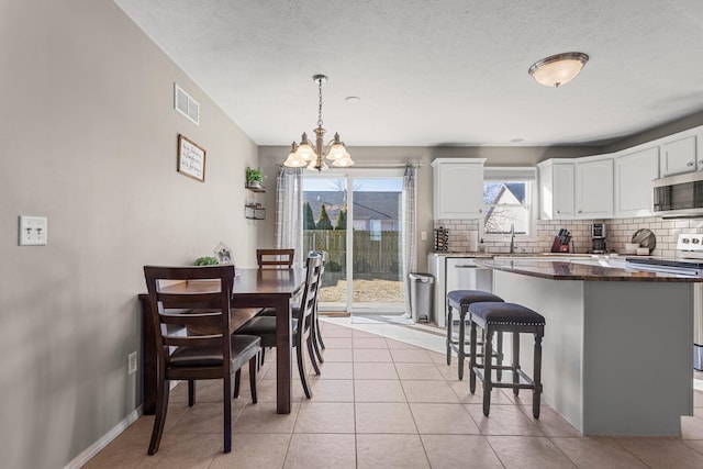 dining space with light tile patterned floors, visible vents, an inviting chandelier, a textured ceiling, and baseboards