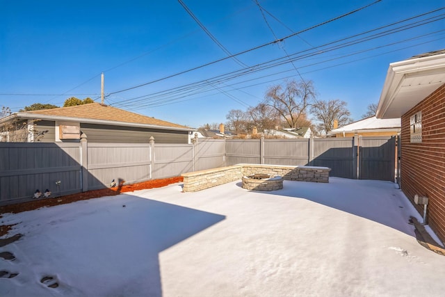 snow covered patio with a fire pit, a fenced backyard, and a gate