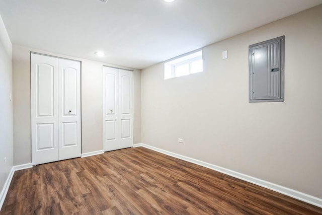 unfurnished bedroom featuring electric panel, baseboards, dark wood finished floors, and two closets