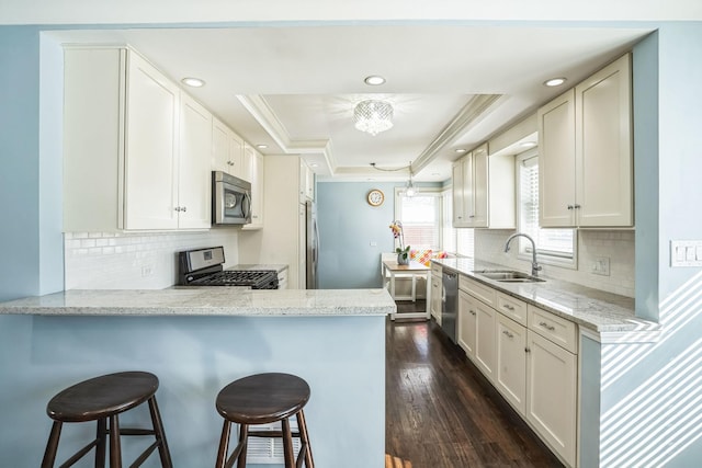 kitchen with stainless steel appliances, a sink, white cabinets, light stone countertops, and a raised ceiling