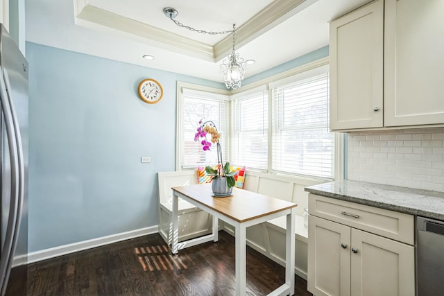 kitchen with light stone counters, hanging light fixtures, appliances with stainless steel finishes, decorative backsplash, and a raised ceiling