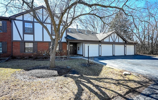 tudor home with a garage, a shingled roof, aphalt driveway, and brick siding