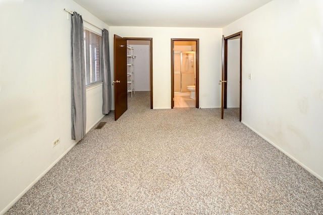 unfurnished bedroom featuring a walk in closet, a closet, light carpet, ensuite bath, and baseboards